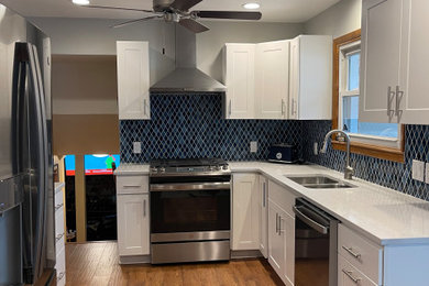 Inspiration for a transitional u-shaped laminate floor and brown floor kitchen remodel in Chicago with a double-bowl sink, shaker cabinets, white cabinets, quartzite countertops, blue backsplash, mosaic tile backsplash, stainless steel appliances, an island and white countertops