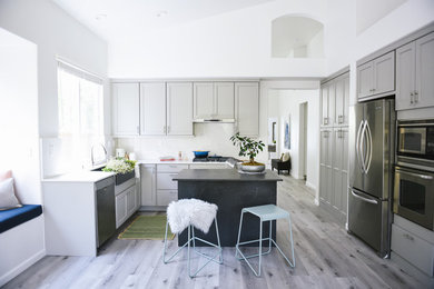 Mid-sized minimalist l-shaped vinyl floor and gray floor eat-in kitchen photo in San Diego with a farmhouse sink, shaker cabinets, gray cabinets, quartz countertops, white backsplash, stone slab backsplash, stainless steel appliances, an island and gray countertops
