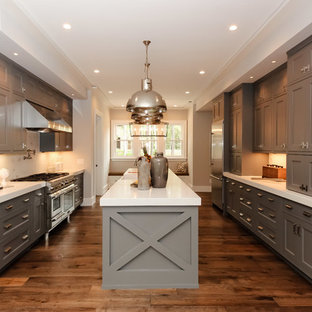 Ejemplo de cocina en U, campestre, de tamaño medio, cerrada, con armarios estilo shaker, puertas de armario grises, salpicadero blanco, electrodomésticos de acero inoxidable, suelo de madera en tonos medios, una isla, fregadero sobremueble y encimera de acrílico
