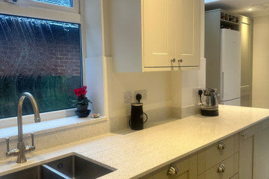 Photo of a medium sized traditional l-shaped kitchen/diner in Surrey with a built-in sink, shaker cabinets, green cabinets, quartz worktops, white splashback, porcelain splashback, stainless steel appliances, vinyl flooring, white floors and white worktops.
