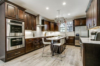 Example of a mid-sized transitional u-shaped light wood floor and beige floor enclosed kitchen design in Dallas with a farmhouse sink, raised-panel cabinets, dark wood cabinets, quartzite countertops, white backsplash, ceramic backsplash, stainless steel appliances and an island