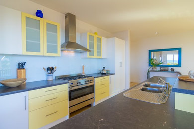 Beach style galley kitchen in Adelaide with a double-bowl sink, flat-panel cabinets, yellow cabinets, laminate benchtops, white splashback, glass sheet splashback, stainless steel appliances, light hardwood floors and with island.