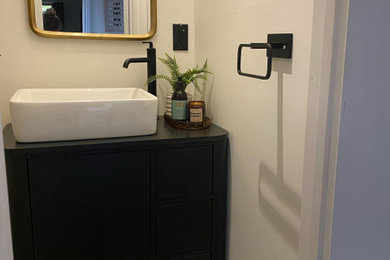Mid-sized trendy porcelain tile and beige floor powder room photo in Other with flat-panel cabinets, black cabinets, gray walls, a vessel sink, wood countertops, black countertops and a floating vanity