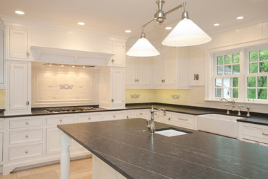 Example of a large classic l-shaped travertine floor eat-in kitchen design in Chicago with a farmhouse sink, beaded inset cabinets, white cabinets, solid surface countertops, white backsplash, glass tile backsplash and an island