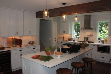 This is an example of a large country u-shaped eat-in kitchen in New York with a farmhouse sink, shaker cabinets, white cabinets, quartz benchtops, white splashback, subway tile splashback, stainless steel appliances, dark hardwood floors and with island.