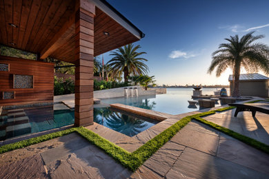 Esempio di una grande piscina a sfioro infinito minimalista personalizzata dietro casa con pavimentazioni in pietra naturale