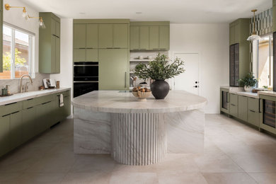 Eat-in kitchen - contemporary u-shaped ceramic tile and beige floor eat-in kitchen idea in Las Vegas with a drop-in sink, flat-panel cabinets, green cabinets, marble countertops, beige backsplash, marble backsplash, black appliances, beige countertops and an island