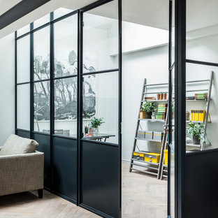 Photo of a contemporary home office and library in London with white walls and light hardwood flooring.