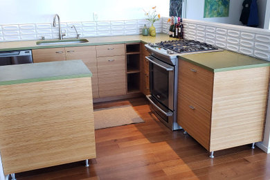 Example of a small 1960s l-shaped medium tone wood floor, brown floor and exposed beam open concept kitchen design in San Francisco with an undermount sink, flat-panel cabinets, medium tone wood cabinets, concrete countertops, white backsplash, subway tile backsplash, stainless steel appliances, a peninsula and green countertops