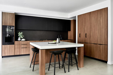 Inspiration for a contemporary l-shaped eat-in kitchen in Sydney with flat-panel cabinets, medium wood cabinets, black splashback, black appliances, with island, grey floor, black benchtop, a double-bowl sink and porcelain floors.