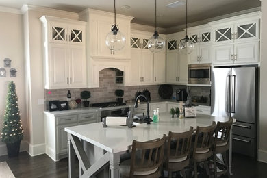 Example of a mid-sized country l-shaped dark wood floor and brown floor open concept kitchen design in Austin with raised-panel cabinets, white cabinets, an island, terrazzo countertops, gray backsplash, stone tile backsplash, stainless steel appliances and a double-bowl sink
