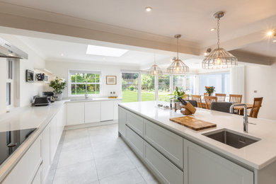 This is an example of a large contemporary u-shaped open plan kitchen in Sussex with white cabinets, quartz worktops, an island and white worktops.