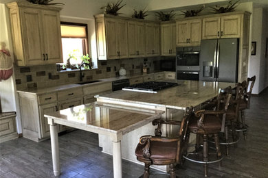 Photo of a rustic l-shaped enclosed kitchen in Kansas City with a submerged sink, raised-panel cabinets, distressed cabinets, granite worktops, multi-coloured splashback, ceramic splashback, stainless steel appliances, porcelain flooring and an island.