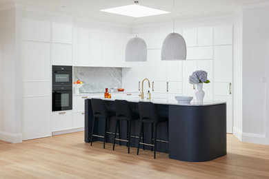 Photo of a mid-sized contemporary open plan kitchen in Sydney with a single-bowl sink, shaker cabinets, white cabinets, marble benchtops, white splashback, marble splashback, black appliances, light hardwood floors, with island, brown floor and white benchtop.