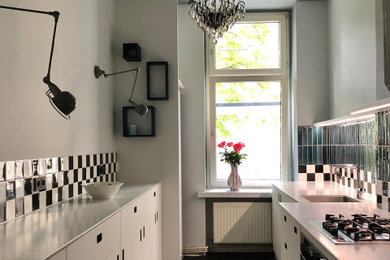 Mittelgroße Stilmix Küche mit Unterbauwaschbecken, flächenbündigen Schrankfronten, weißen Schränken, Mineralwerkstoff-Arbeitsplatte und schwarzem Boden in Berlin