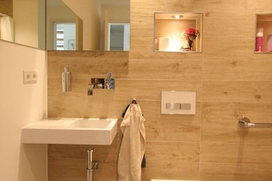 Großes Modernes Badezimmer En Suite mit offenen Schränken, weißen Schränken, Einbaubadewanne, bodengleicher Dusche, Wandtoilette, Travertinfliesen, weißer Wandfarbe, Kiesel-Bodenfliesen, Wandwaschbecken, buntem Boden und offener Dusche in Köln