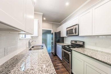 Photo of a large transitional galley separate kitchen in Other with a double-bowl sink, shaker cabinets, white cabinets, granite benchtops, white splashback, subway tile splashback, stainless steel appliances, dark hardwood floors, no island and brown floor.