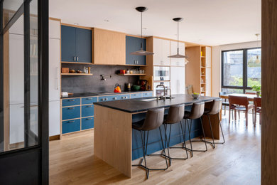 1960s galley light wood floor and beige floor kitchen photo in Toronto with an undermount sink, flat-panel cabinets, blue cabinets, gray backsplash, stainless steel appliances, an island and black countertops