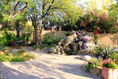 This is an example of a mid-sized mediterranean backyard partial sun xeriscape for spring in Phoenix with a water feature and brick pavers.