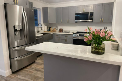 Open concept kitchen - small traditional galley medium tone wood floor, beige floor and tray ceiling open concept kitchen idea in Miami with a drop-in sink, shaker cabinets, gray cabinets, quartz countertops, stainless steel appliances, an island and white countertops