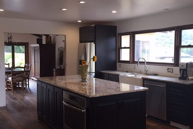 Inspiration for a large transitional galley dark wood floor eat-in kitchen remodel in San Francisco with a farmhouse sink, raised-panel cabinets, black cabinets, granite countertops, stainless steel appliances and an island