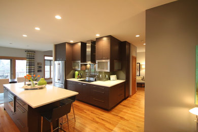Example of a mid-sized trendy light wood floor and brown floor kitchen design in Other with an undermount sink, flat-panel cabinets, dark wood cabinets, quartz countertops, gray backsplash, glass tile backsplash, stainless steel appliances and an island