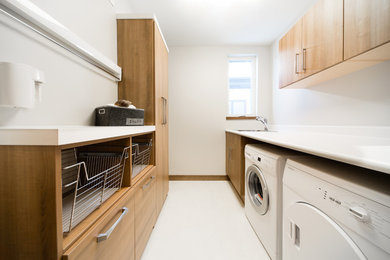 Inspiration for a large contemporary galley vinyl floor dedicated laundry room remodel in Other with a single-bowl sink, white walls, a side-by-side washer/dryer, flat-panel cabinets and medium tone wood cabinets