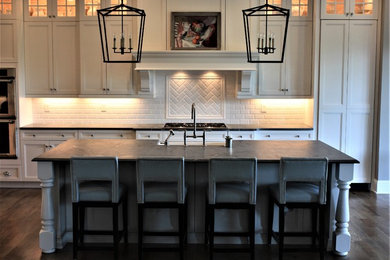 Example of a transitional dark wood floor and brown floor open concept kitchen design in Cincinnati with a farmhouse sink, recessed-panel cabinets, white cabinets, soapstone countertops, white backsplash, subway tile backsplash, stainless steel appliances and an island