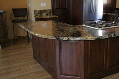 Example of a mid-sized classic single-wall light wood floor and beige floor open concept kitchen design in San Diego with raised-panel cabinets, dark wood cabinets, granite countertops, beige backsplash, stone slab backsplash, stainless steel appliances and a peninsula