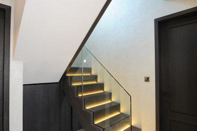 ロンドンにある高級なコンテンポラリースタイルのおしゃれな階段 (木の蹴込み板、ガラスフェンス) の写真