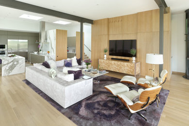 Modelo de salón abierto minimalista grande sin chimenea con paredes blancas, suelo de madera clara, televisor colgado en la pared, suelo beige y vigas vistas