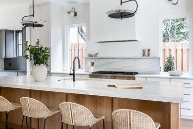Kitchen - transitional light wood floor kitchen idea in Austin with an undermount sink, white cabinets, quartzite countertops, white backsplash, stone slab backsplash, stainless steel appliances, an island and white countertops