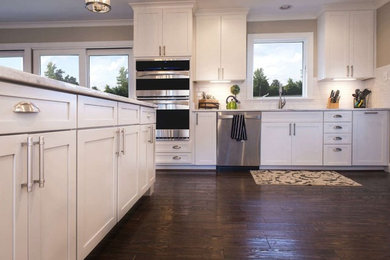Inspiration for a large transitional u-shaped dark wood floor kitchen remodel in St Louis with recessed-panel cabinets, white cabinets, solid surface countertops, white backsplash, subway tile backsplash and stainless steel appliances