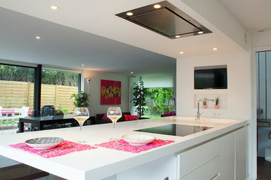 Cette photo montre une grande cuisine américaine parallèle et encastrable tendance avec un placard à porte plane, des portes de placard blanches, un plan de travail en surface solide, îlot et un évier intégré.