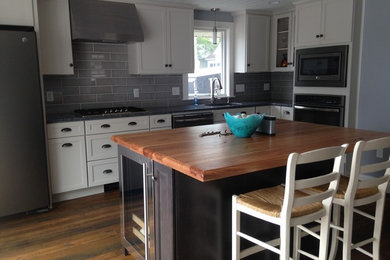 Example of a mid-sized u-shaped medium tone wood floor eat-in kitchen design in Boston with an undermount sink, recessed-panel cabinets, white cabinets, gray backsplash, stainless steel appliances and an island