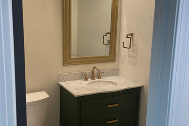 Powder room - small transitional light wood floor and brown floor powder room idea in Atlanta with furniture-like cabinets, green cabinets, a two-piece toilet, white walls, an undermount sink, marble countertops, white countertops and a freestanding vanity