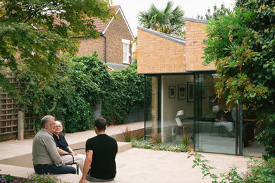 Photo of a large midcentury back formal partial sun garden for summer in Surrey with natural stone paving and a wood fence.