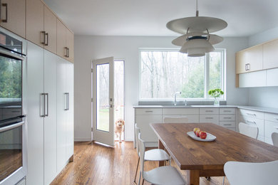 This is an example of a large midcentury u-shaped kitchen in Boston with an undermount sink, flat-panel cabinets, yellow cabinets, white splashback, stainless steel appliances, medium hardwood floors, no island, brown floor and grey benchtop.