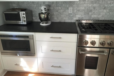 Mid-sized transitional medium tone wood floor and brown floor kitchen pantry photo in New York with shaker cabinets, white cabinets, solid surface countertops, gray backsplash, marble backsplash, stainless steel appliances and no island