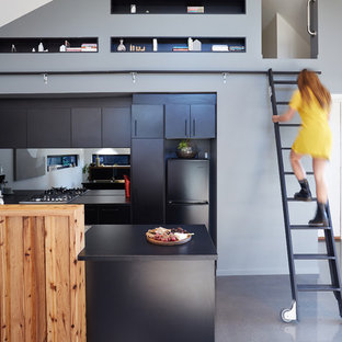 メルボルンのコンテンポラリースタイルのおしゃれなキッチン (フラットパネル扉のキャビネット、黒いキャビネット、メタリックのキッチンパネル、ミラータイルのキッチンパネル、黒い調理設備、コンクリートの床) の写真