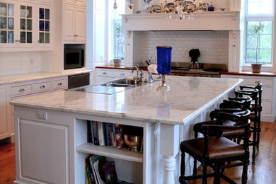 Example of a classic l-shaped light wood floor open concept kitchen design in Other with raised-panel cabinets, white cabinets, marble countertops, white backsplash, subway tile backsplash, stainless steel appliances and an island
