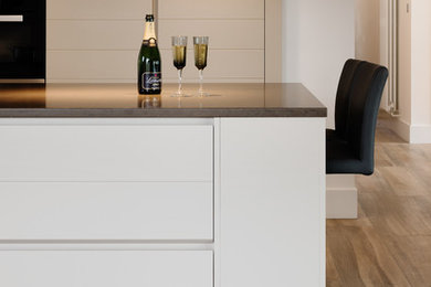 Large contemporary l-shaped open plan kitchen in Devon with flat-panel cabinets, grey cabinets, quartz worktops, light hardwood flooring and an island.