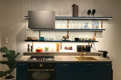 Imagen de cocina actual pequeña abierta sin isla con puertas de armario azules, encimera de cemento, salpicadero verde y encimeras grises