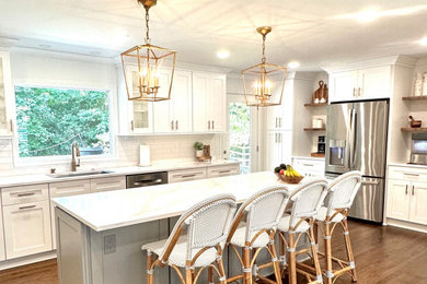Example of a large trendy l-shaped medium tone wood floor, brown floor and coffered ceiling open concept kitchen design in Atlanta with a drop-in sink, flat-panel cabinets, white cabinets, quartz countertops, white backsplash, subway tile backsplash, stainless steel appliances, an island and white countertops