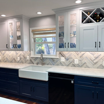 White upper cabinets with blue base cabinets with herringbone tile backsplash