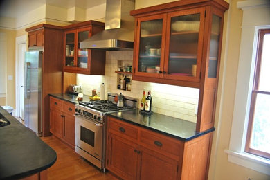 Mid-sized transitional l-shaped eat-in kitchen in San Diego with a double-bowl sink, recessed-panel cabinets, medium wood cabinets, granite benchtops, white splashback, subway tile splashback, stainless steel appliances, medium hardwood floors, with island and brown floor.