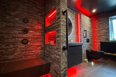 Large urban master gray tile and porcelain tile porcelain tile, gray floor and single-sink wet room photo in Dorset with black cabinets, a bidet, black walls, a wall-mount sink, solid surface countertops, black countertops, a niche and a floating vanity