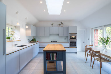 Large country open plan kitchen in London with a drop-in sink, beaded inset cabinets, grey cabinets, wood benchtops, white splashback, panelled appliances, porcelain floors and with island.