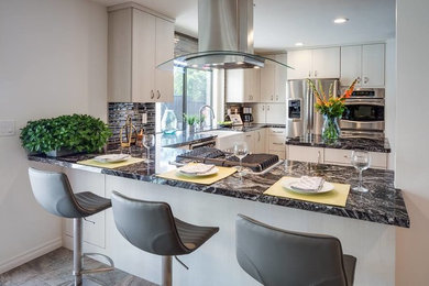 Inspiration for an u-shaped porcelain tile and gray floor kitchen pantry remodel in San Diego with a farmhouse sink, flat-panel cabinets, white cabinets, granite countertops, black backsplash, glass tile backsplash, stainless steel appliances and an island