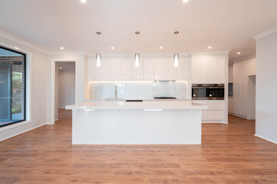 This is an example of a contemporary kitchen in Melbourne with an undermount sink, white splashback, glass sheet splashback, stainless steel appliances, laminate floors, with island and white benchtop.